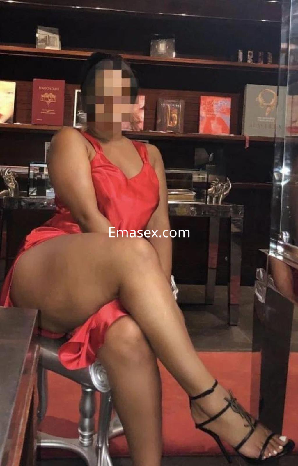 Escort en Almería luciendo un vestido rojo, sentada con una pierna cruzada en un entorno elegante.