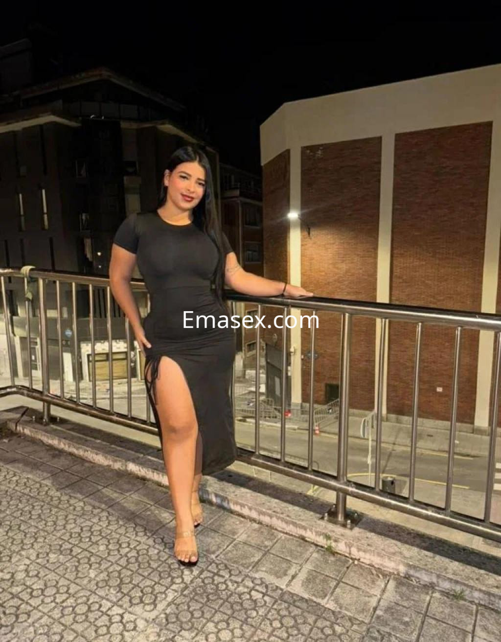 La puta viste un vestido negro ajustado con una abertura lateral, posando en un balcón de Pontevedra.