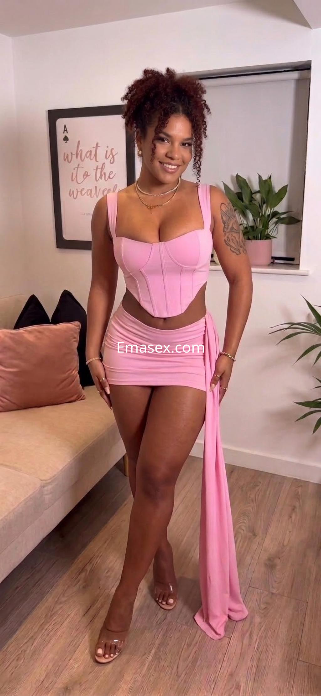Escort en Ibiza con cabello rizado y oscuro, viste un conjunto rosa con top ajustado y falda corta.