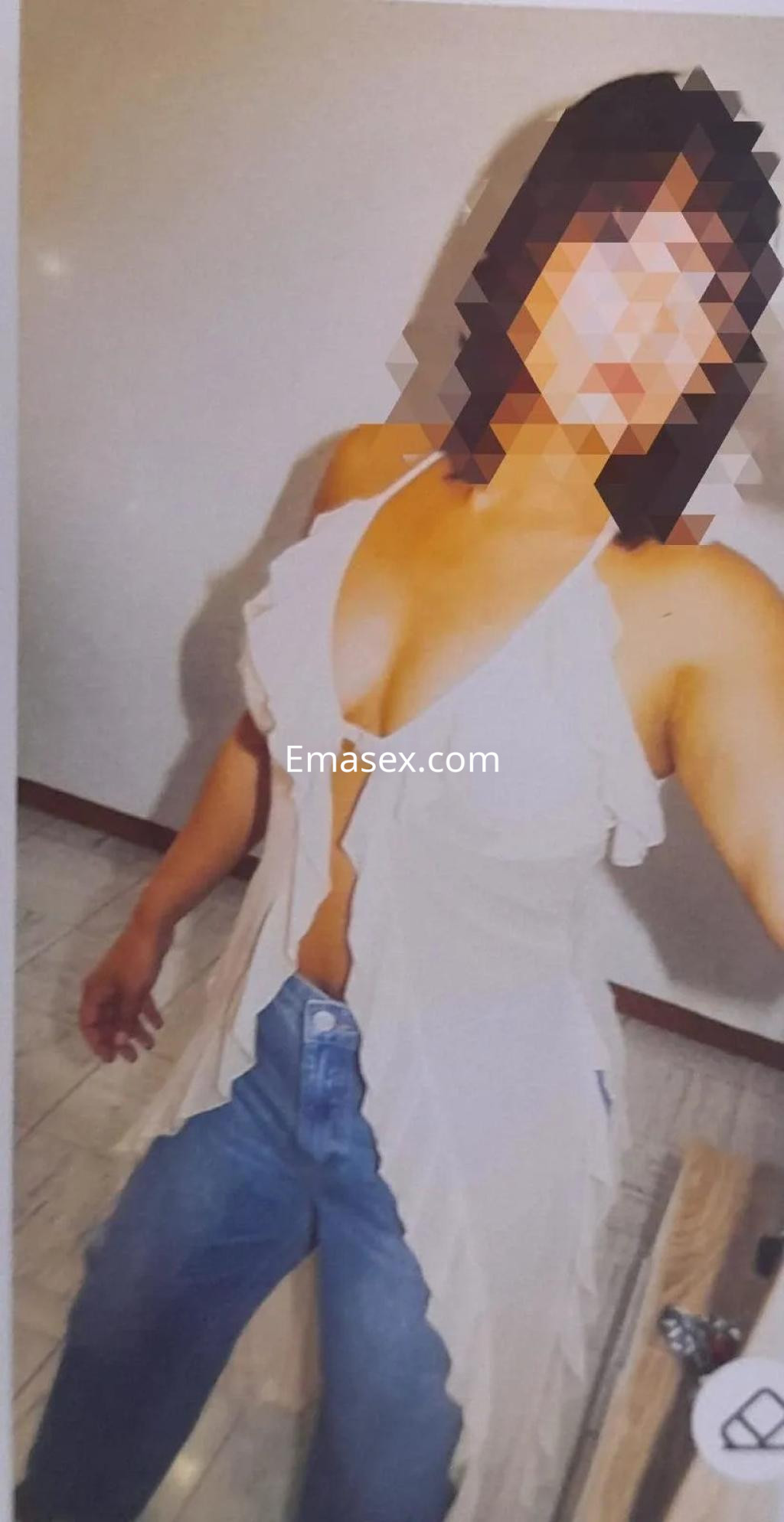 Escort en Vigo posando frente al espejo, viste una blusa blanca con volantes y jeans ajustados.
