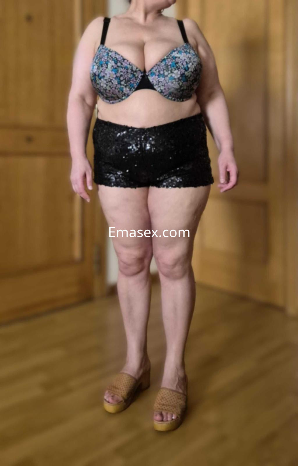 Puta en Zaragoza luciendo un sujetador floral y shorts brillantes, de pie en un ambiente interior.