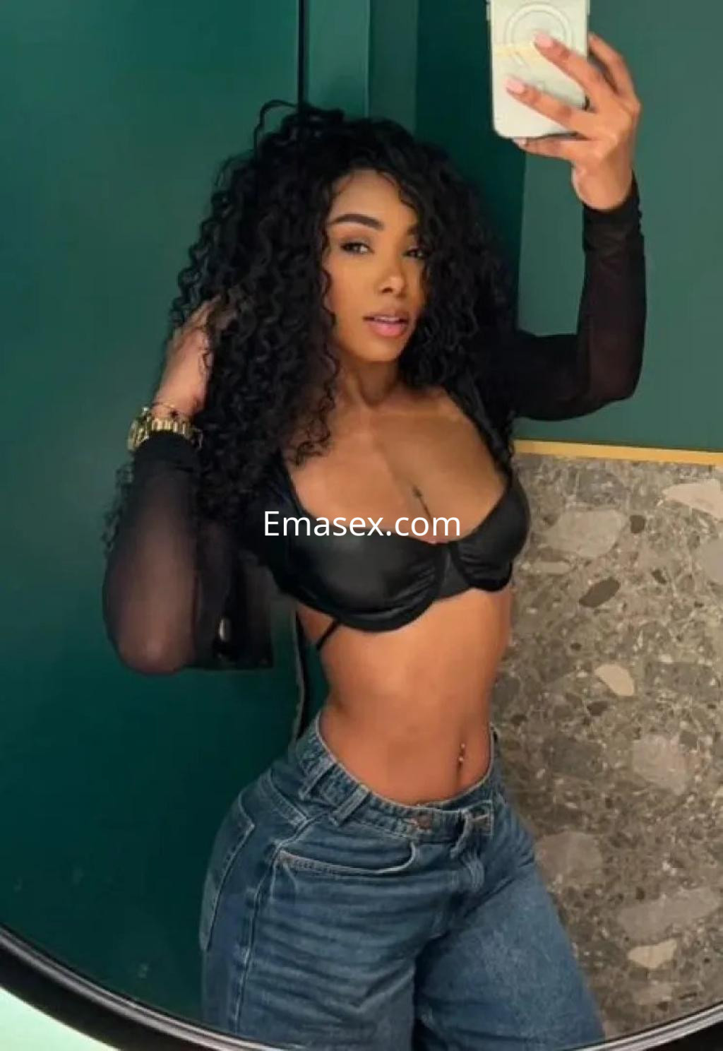 Escort en Córdoba posando en un espejo con top negro de cuero y jeans, luciendo cabello rizado y maquillaje sutil.