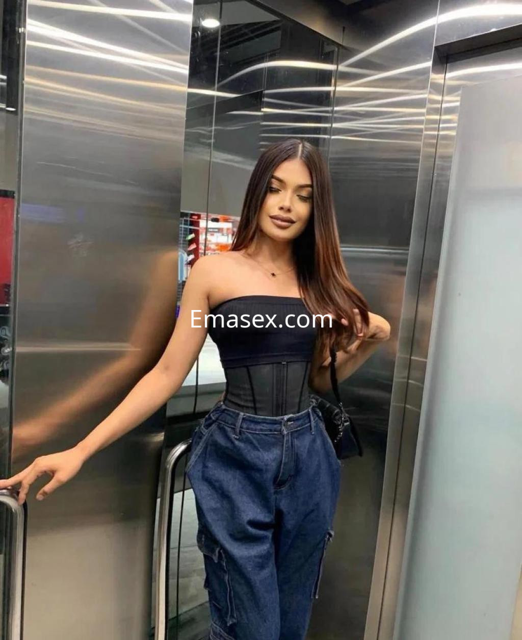 Puta en Castellón, posa en un ascensor con blusa negra ajustada y pantalones de mezclilla, cabello largo y lacio.