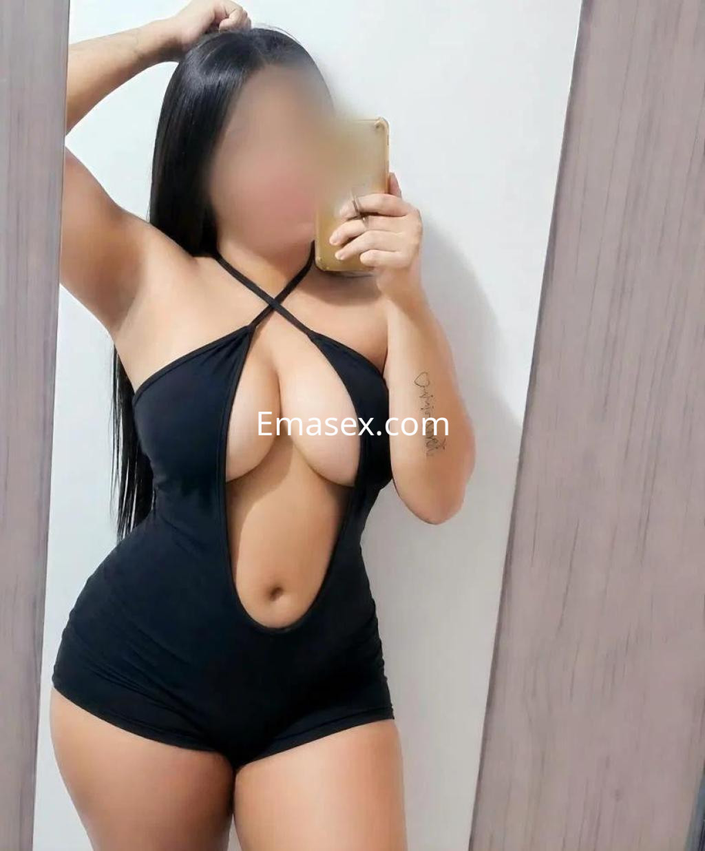Escort en Córdoba, posando frente a un espejo con un mono negro que resalta su figura y cabello largo.