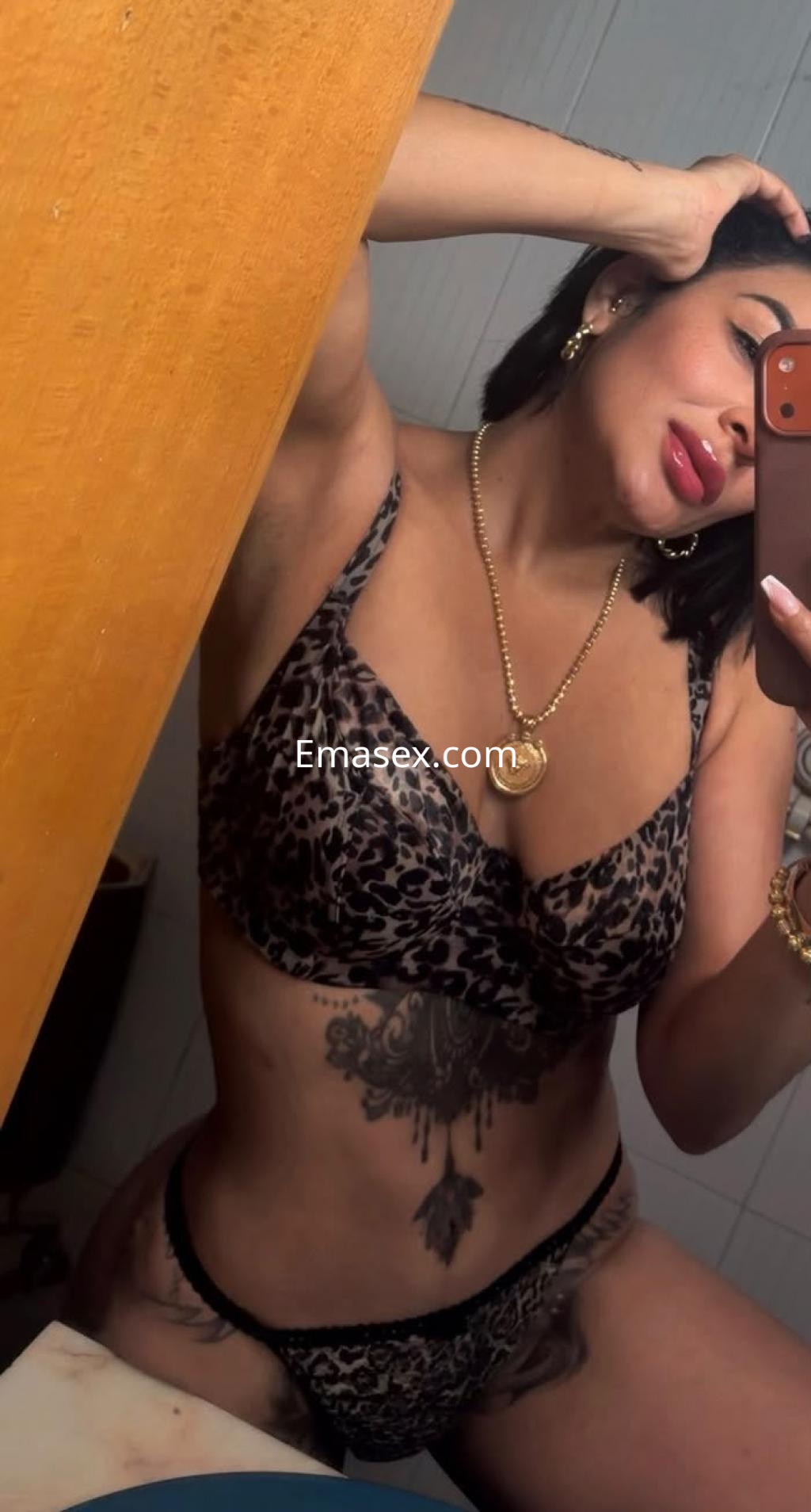 Escort en Gijón posando en un lavabo, lleva un conjunto de lencería animal print y accesorios dorados.