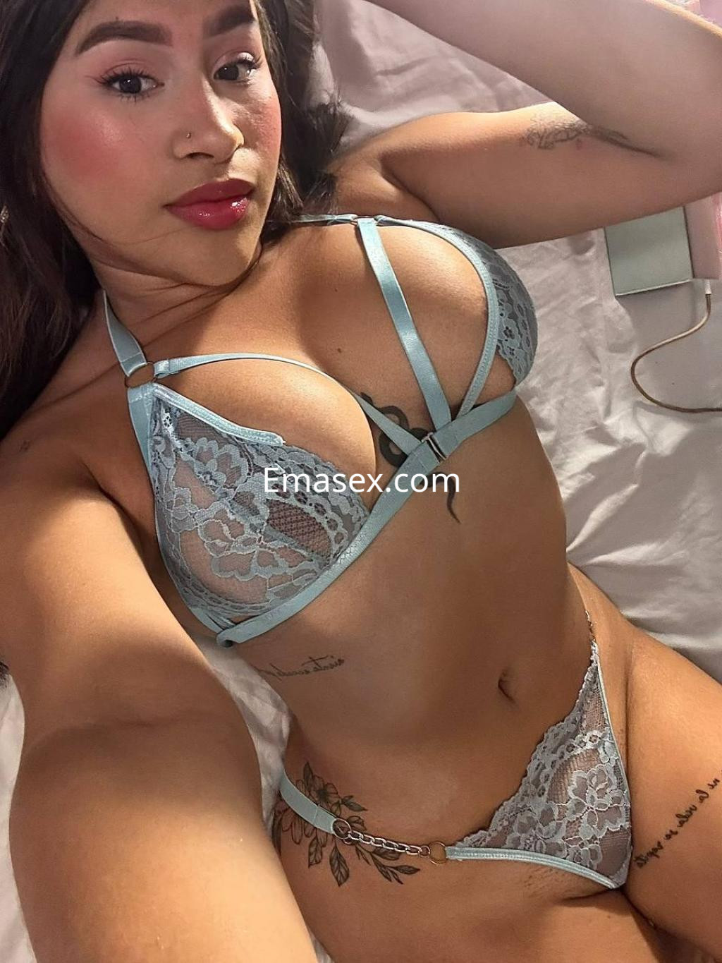 Escort en Donosti posando en lencería azul claro, con cabello oscuro y labios rojos, sobre una cama.