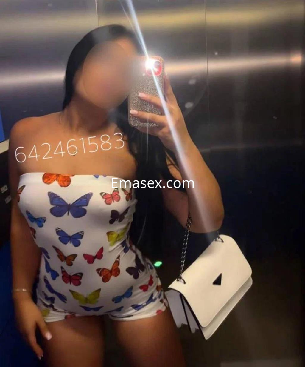 Puta en Cáceres, posando en un ascensor con un mono sin mangas de mariposas y un bolso blanco.
