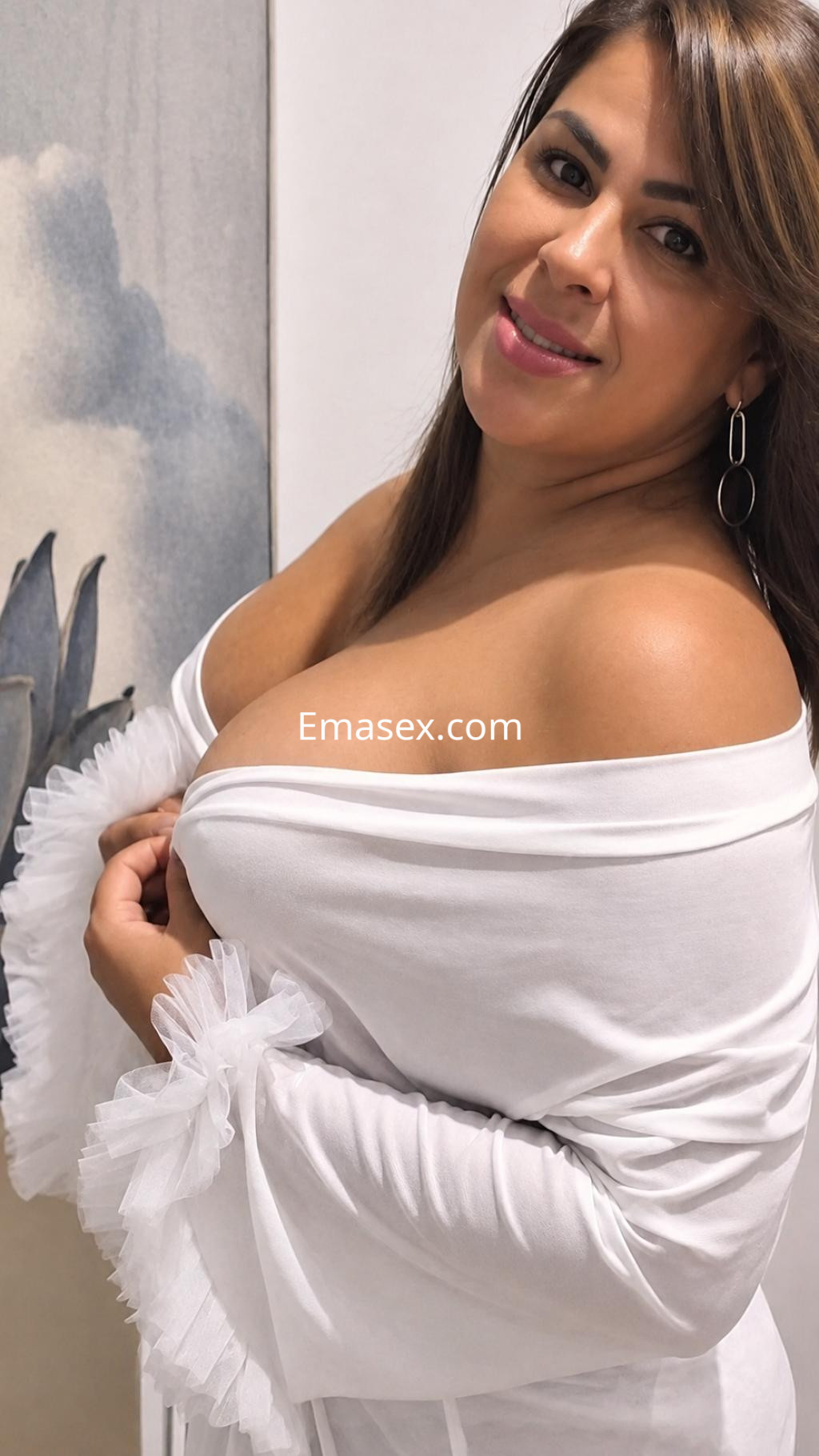 Puta de cabello castaño y lacio, viste una blusa blanca con detalles en tul y sonríe en un entorno decorativo en Vitoria.