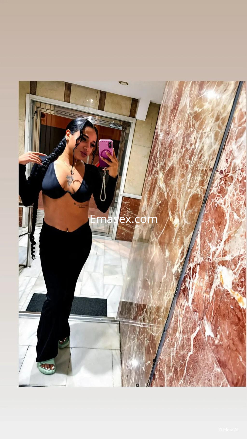 Escort en Zaragoza posando en un espejo, luciendo un top negro y pantalones ajustados, con cabello trenzado.