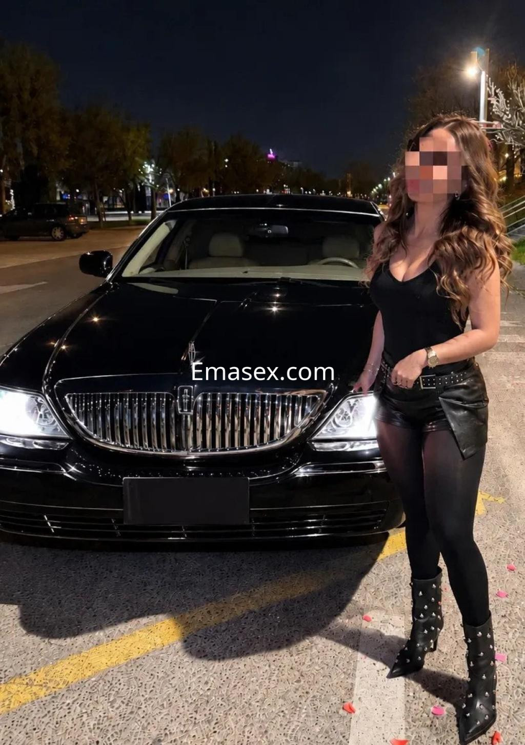 La puta posando junto a un coche negro, viste una blusa ajustada y pantalones cortos de cuero en Zaragoza.