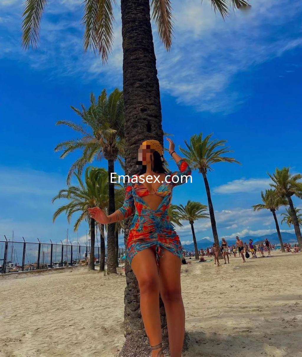 La puta posa junto a una palmera en la playa de Las Palmas, luciendo un vestido colorido y veraniego.