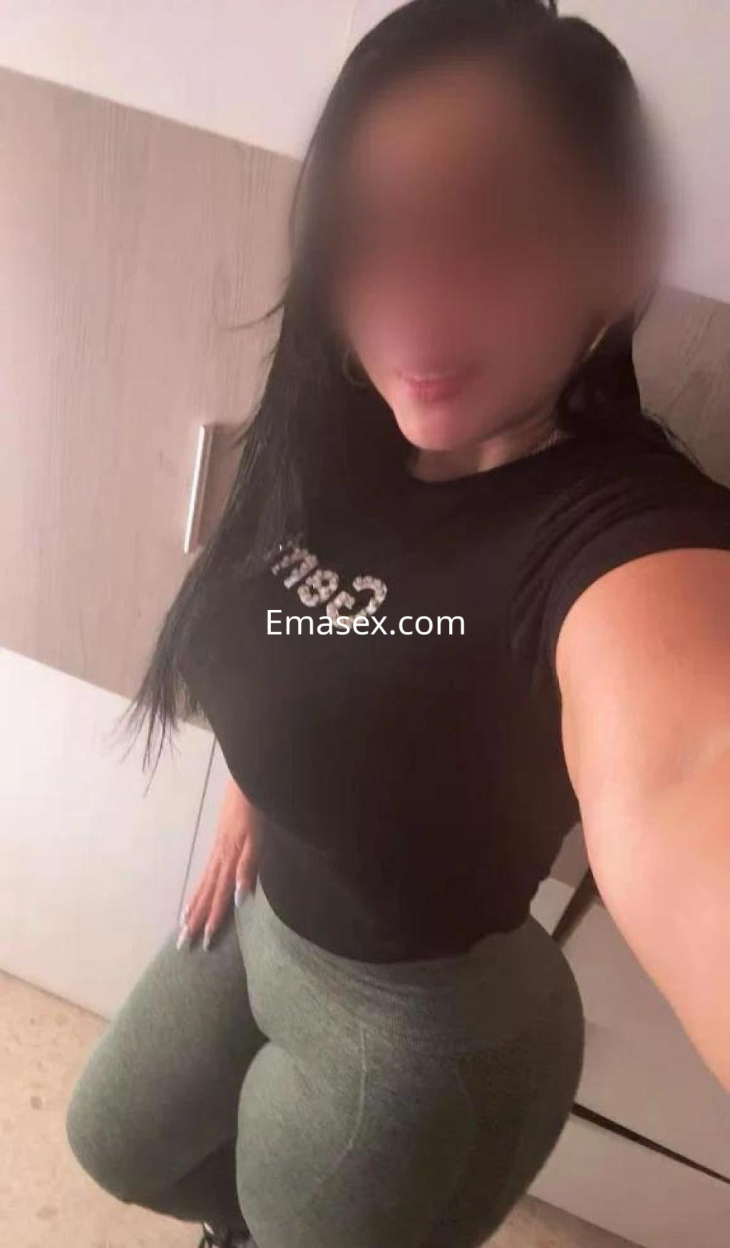 Escort en Badajoz con cabello largo y oscuro, vistiendo camiseta negra y leggins verdes, posando de perfil.