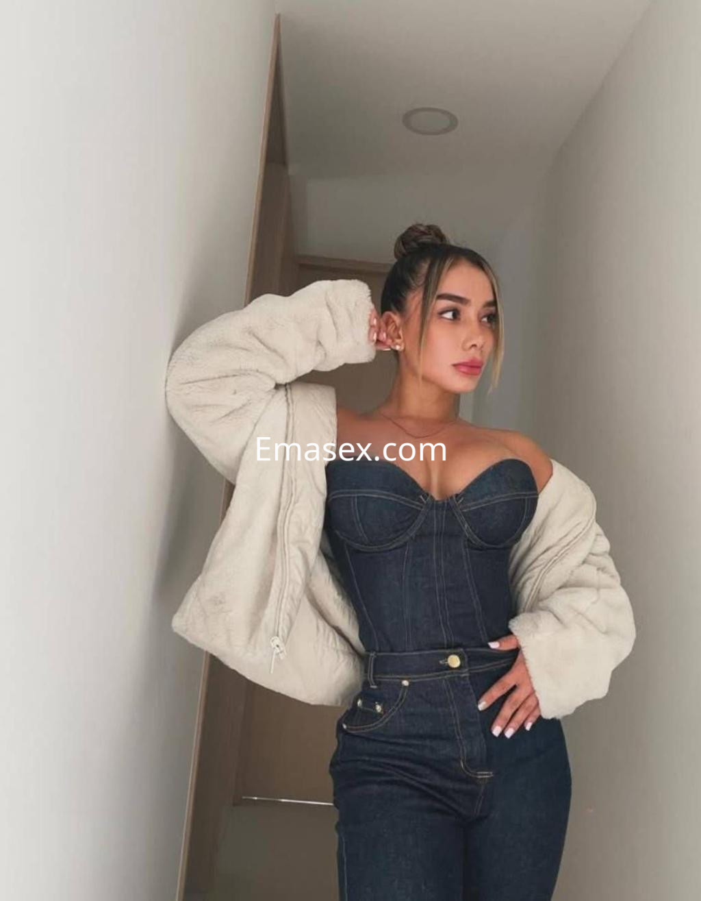 Puta posando en un vestidor con un conjunto ajustado de mezclilla, chaqueta clara y cabello recogido en Zaragoza.