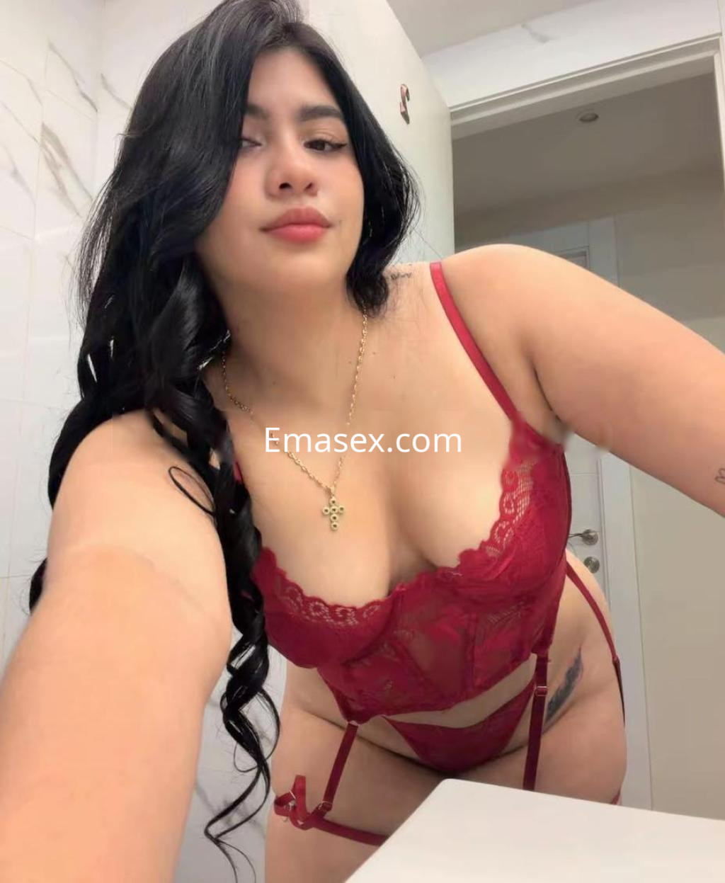Escort en Girona posando con lencería roja, cabello largo y ondulado, en un entorno de baño.
