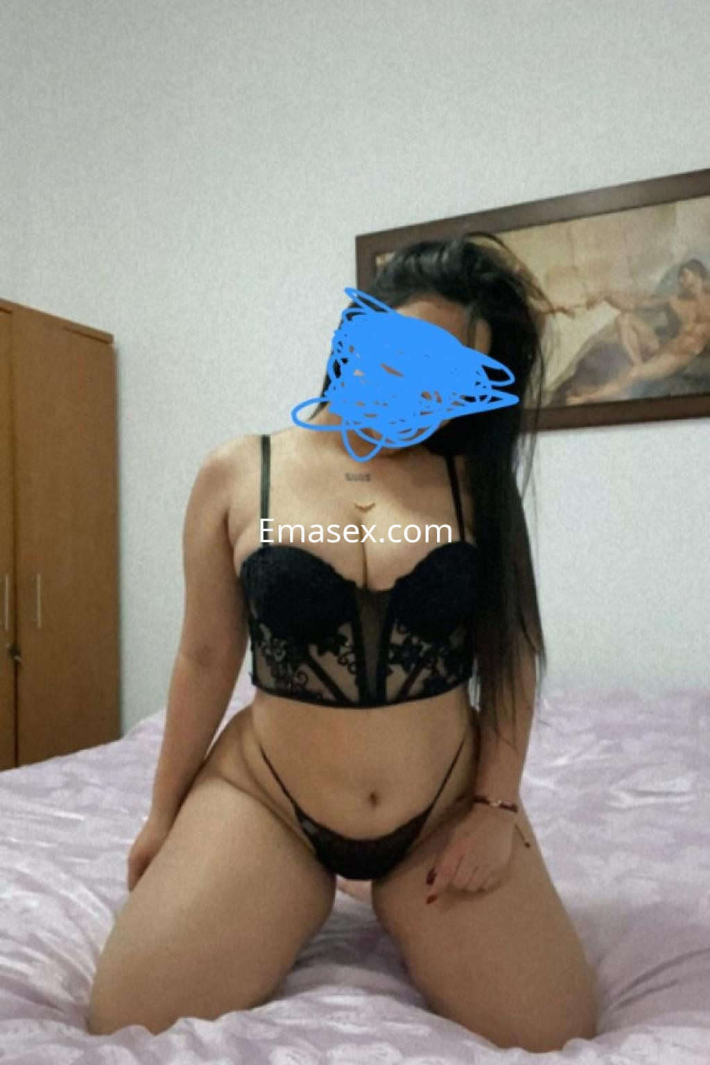 Escort en Coruña, posando en lencería negra en una habitación con decoración sencilla y luz suave.