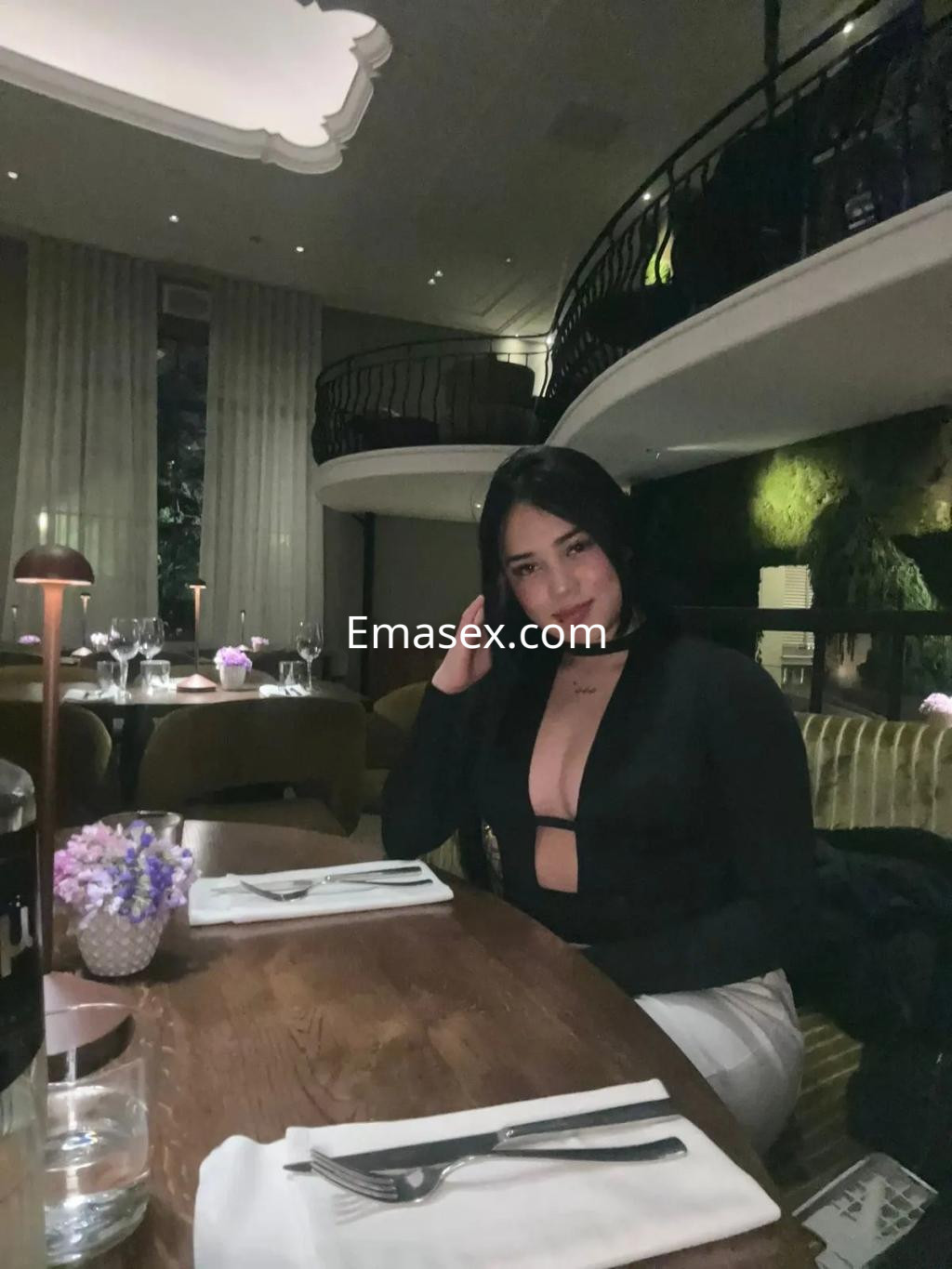 La puta viste un top negro con escote y se encuentra sentada en una mesa elegante en Zaragoza.