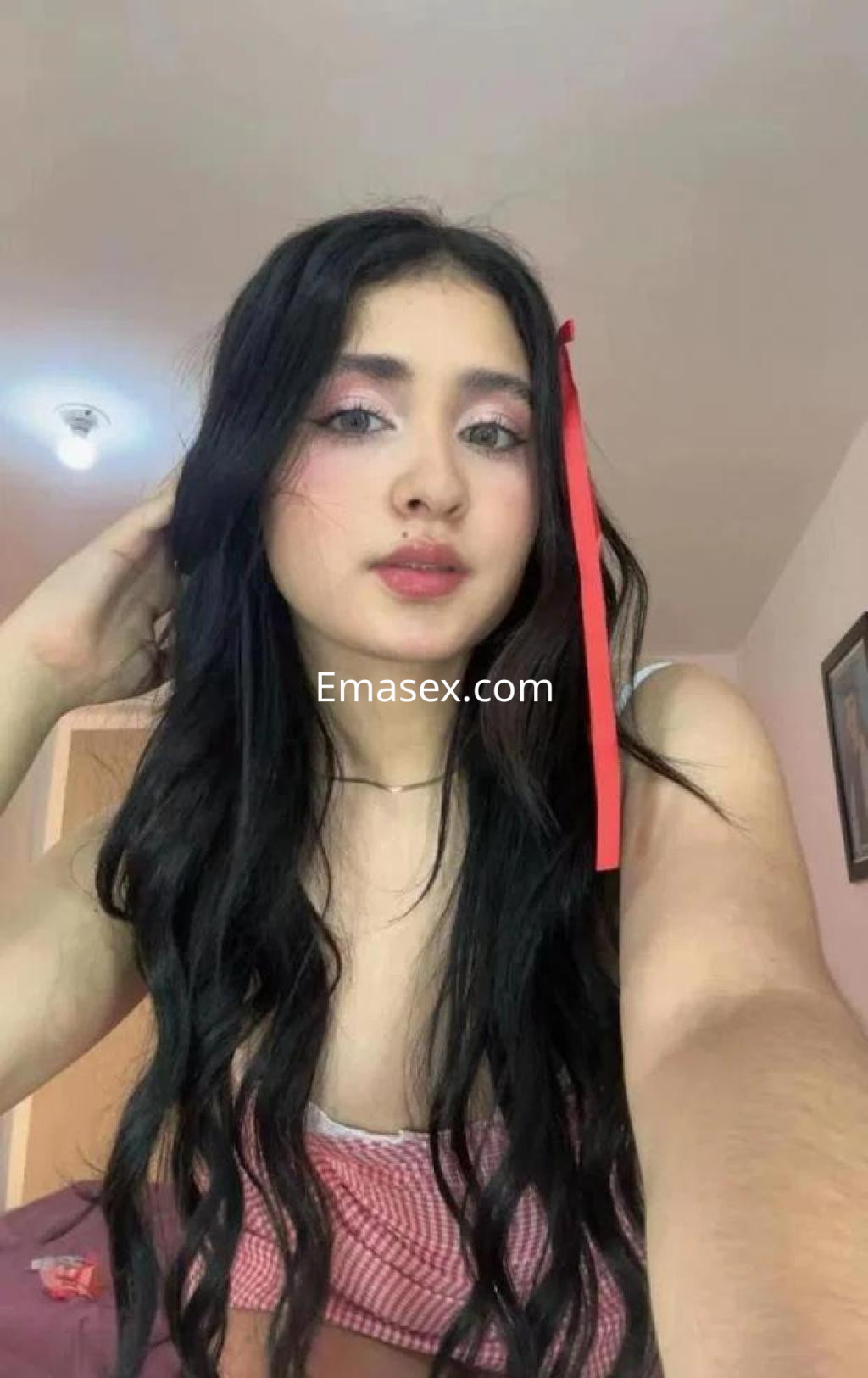 Escort en Coruña con cabello largo y oscuro, usando un top blanco, maquillaje suave y una cinta roja en el pelo.