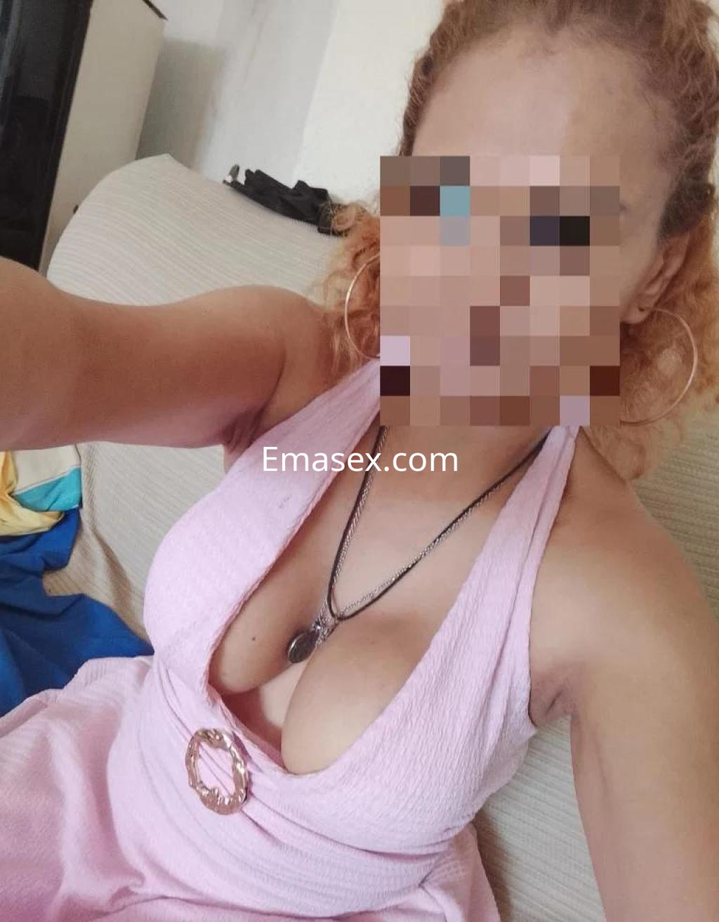 Escort en Castellón con cabello rizado y rubio, viste un vestido rosa con escote y joyería.