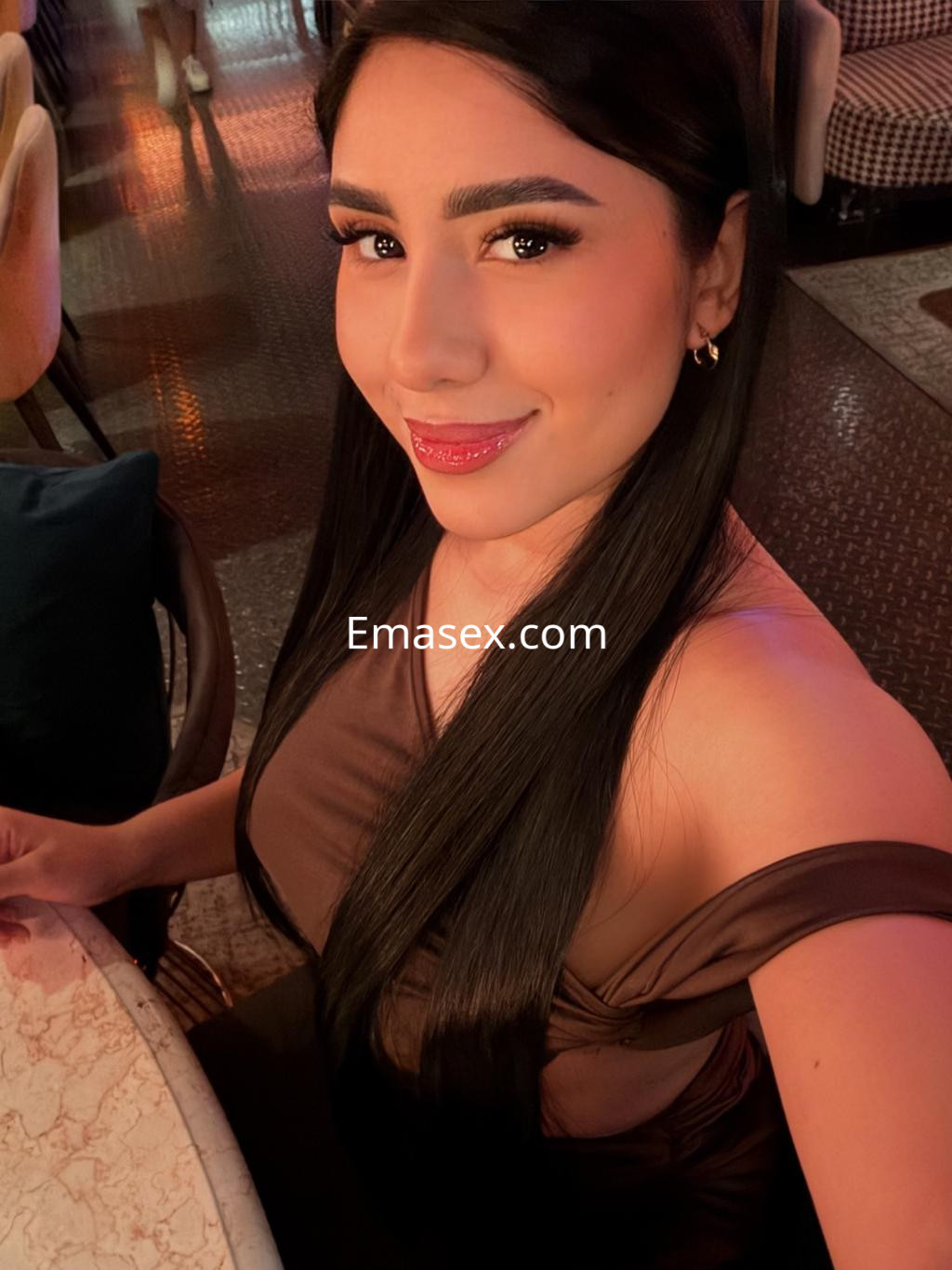 Escort en Vigo con cabello largo y lacio, vistiendo una blusa marrón, sonriendo en un entorno elegante.