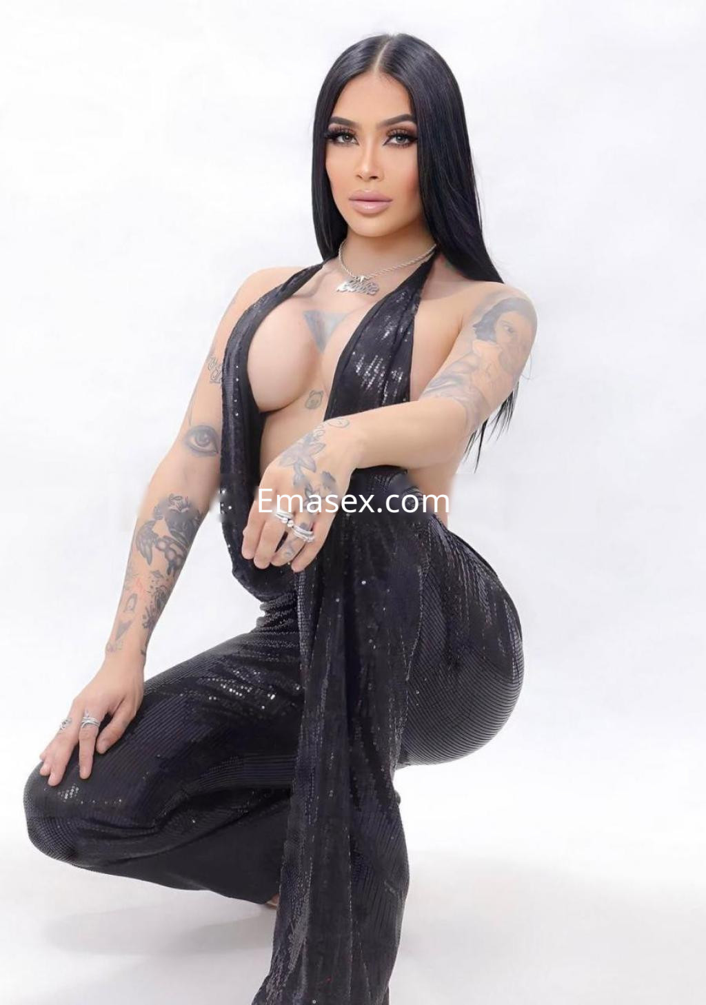 La puta en Lleida luce un conjunto negro brillante y ajustado, posando con confianza y mostrando sus tatuajes.