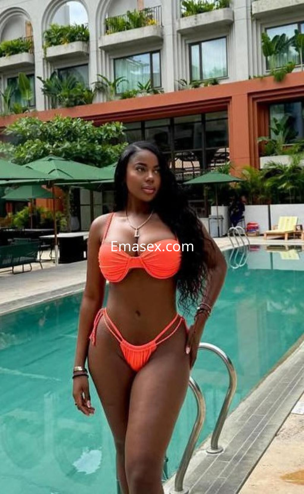 Puta de piel oscura luciendo un bikini naranja y posando con confianza junto a una piscina en Girona.