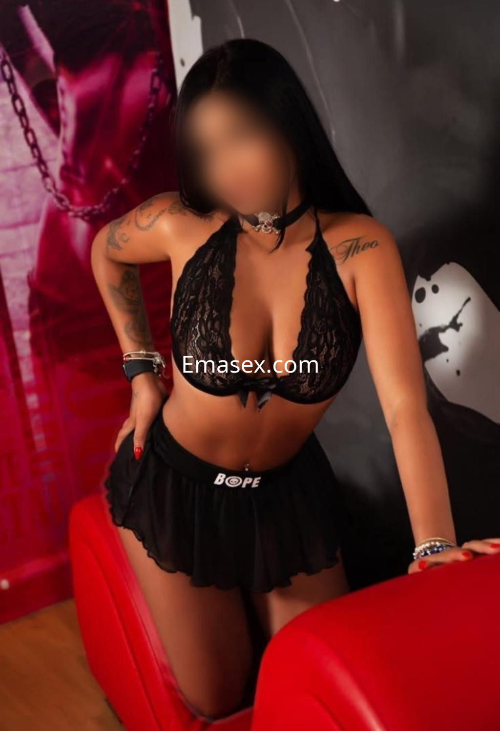 Puta en Donosti luce un conjunto de lencería negra con encaje, posando de forma seductora sobre un sofá rojo.