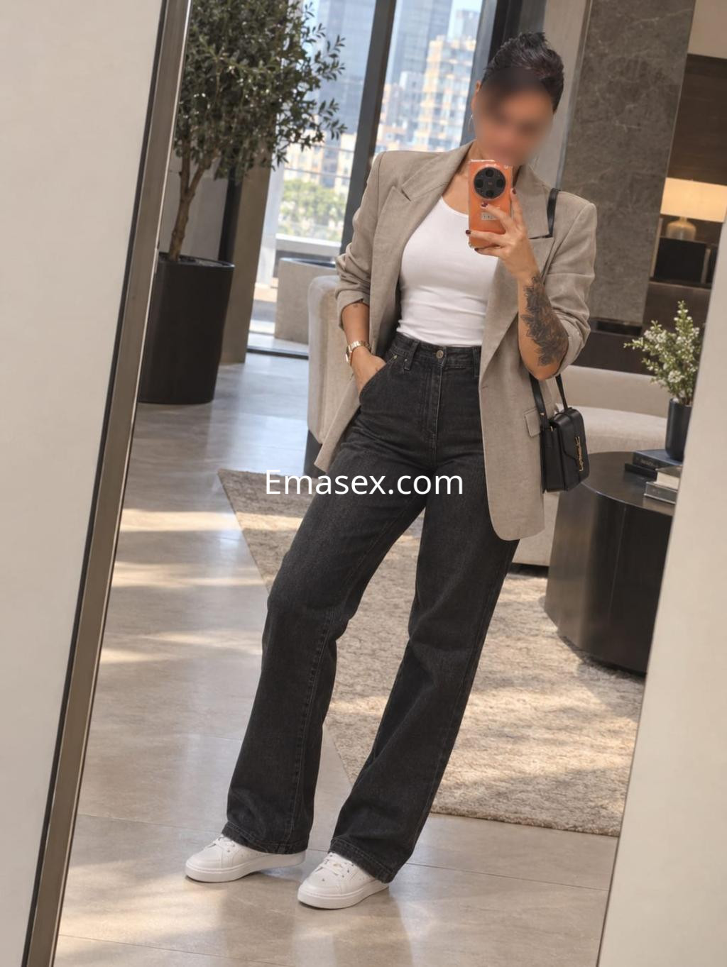 Escort en Bilbao con blusa blanca y blazer gris, luciendo jeans oscuros y zapatillas blancas en un entorno moderno.