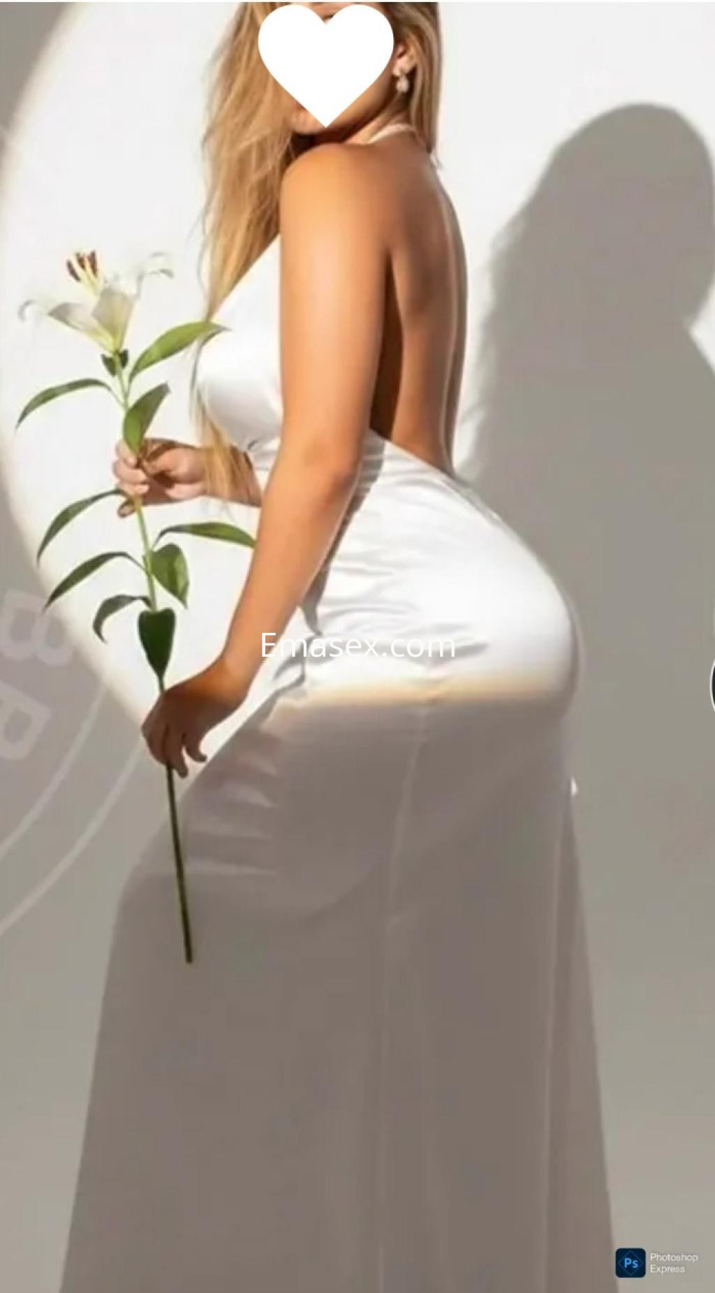 Escort en Coruña posa de espaldas con un vestido blanco sin mangas, sosteniendo una flor.