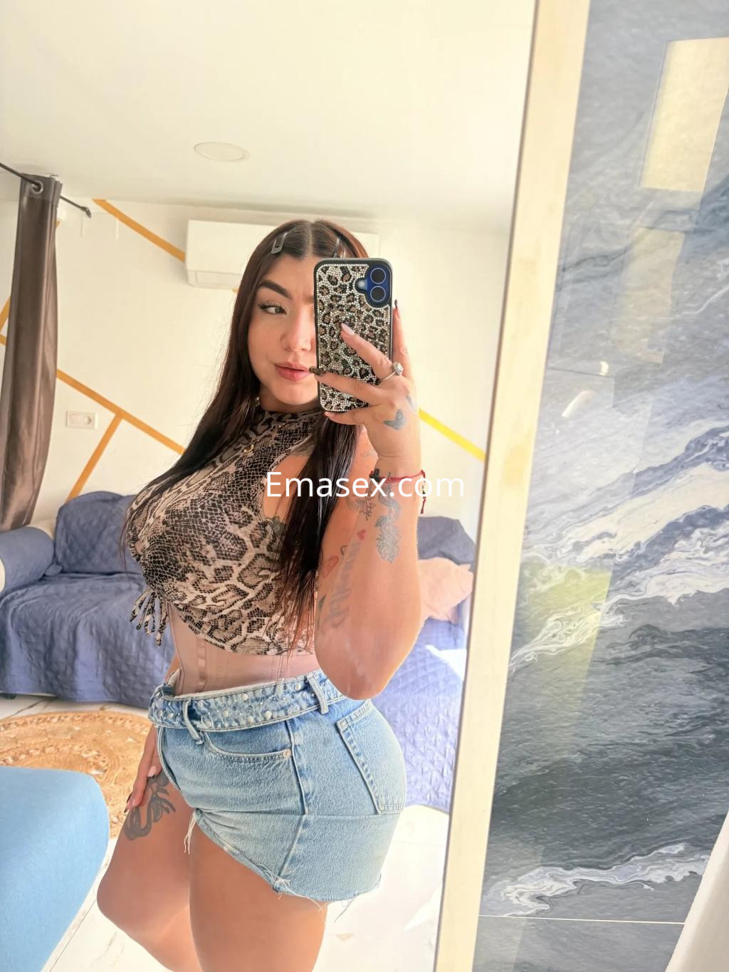 Puta en Zaragoza posa frente al espejo con blusa de estampado animal y short de mezclilla, mostrando su figura.