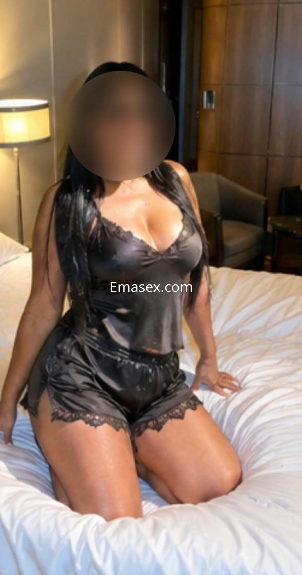 Escort en Lugo, con un conjunto de lencería negra, sentada sobre una cama en un entorno elegante y acogedor.