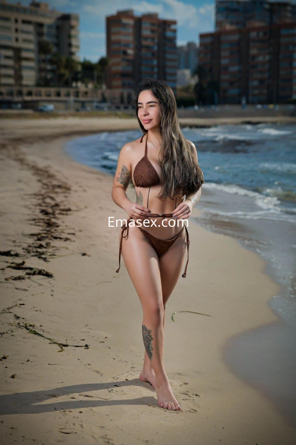 Puta en Málaga camina por la playa luciendo un bikini marrón y exhibiendo sus tatuajes en la piel.