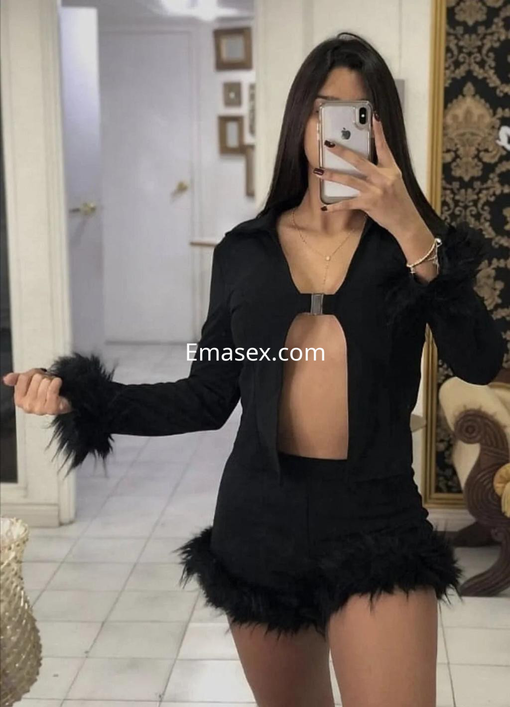Escort en Gijón con un conjunto negro de tela suave y detalles de plumas, posando frente a un espejo.