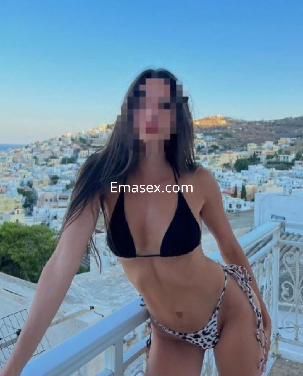 Escort en Pamplona con cabello largo y oscuro, vistiendo un bikini negro y una parte inferior de leopardo, en un balcón con vista.