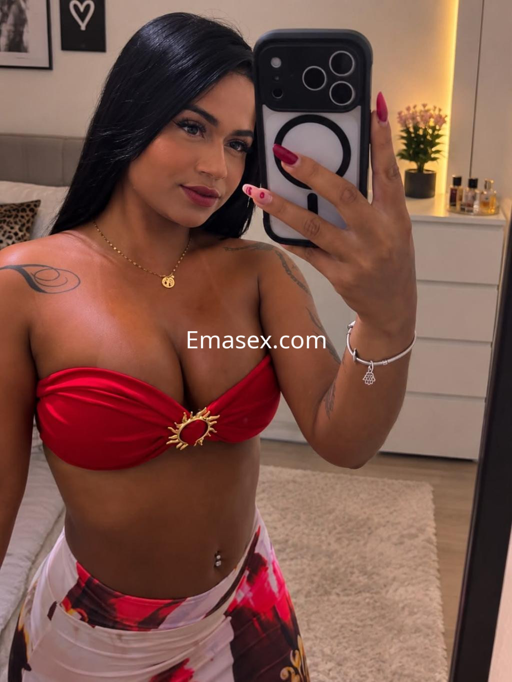 Escort en Donosti, luciendo un top rojo que realza su figura y una falda estampada, posando frente al espejo.