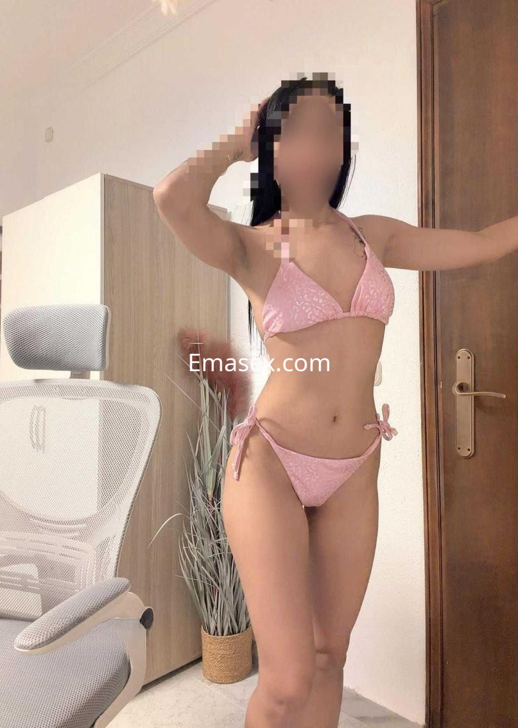 Escort en Málaga posando en bikini rosa, con cabello oscuro, en un ambiente interior moderno.