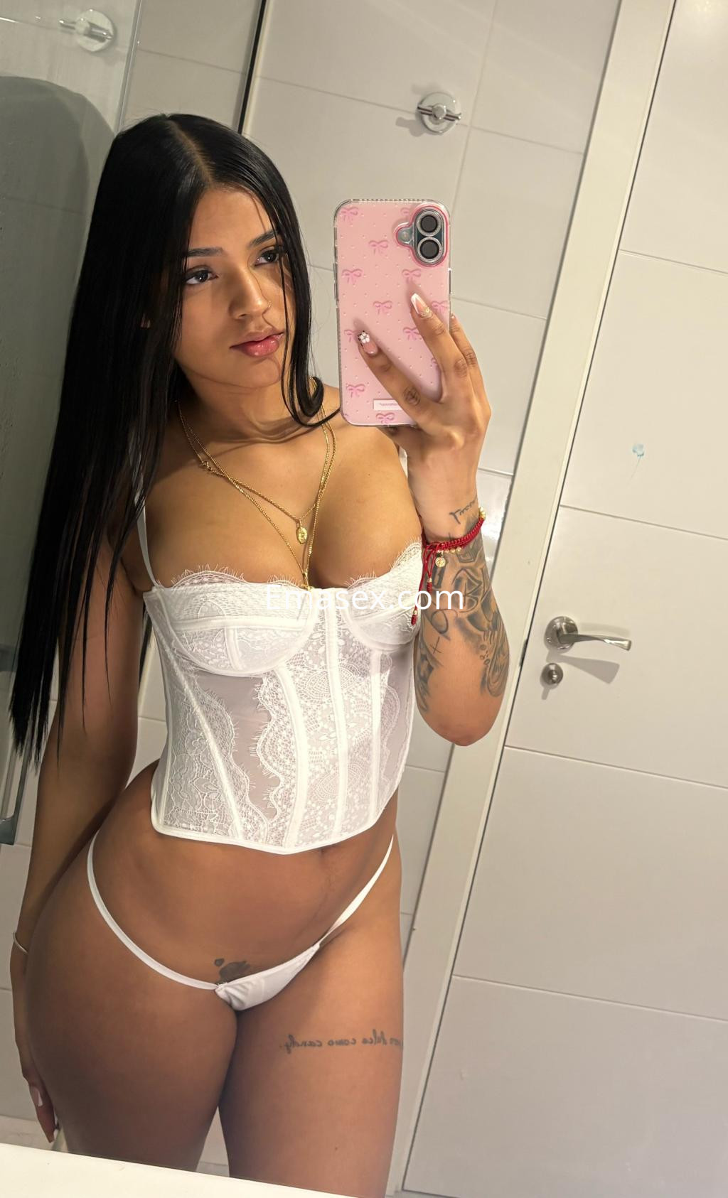 Escort en Vitoria, con cabello largo y lacio, vistiendo un corset blanco y tanga, posando frente a un espejo.