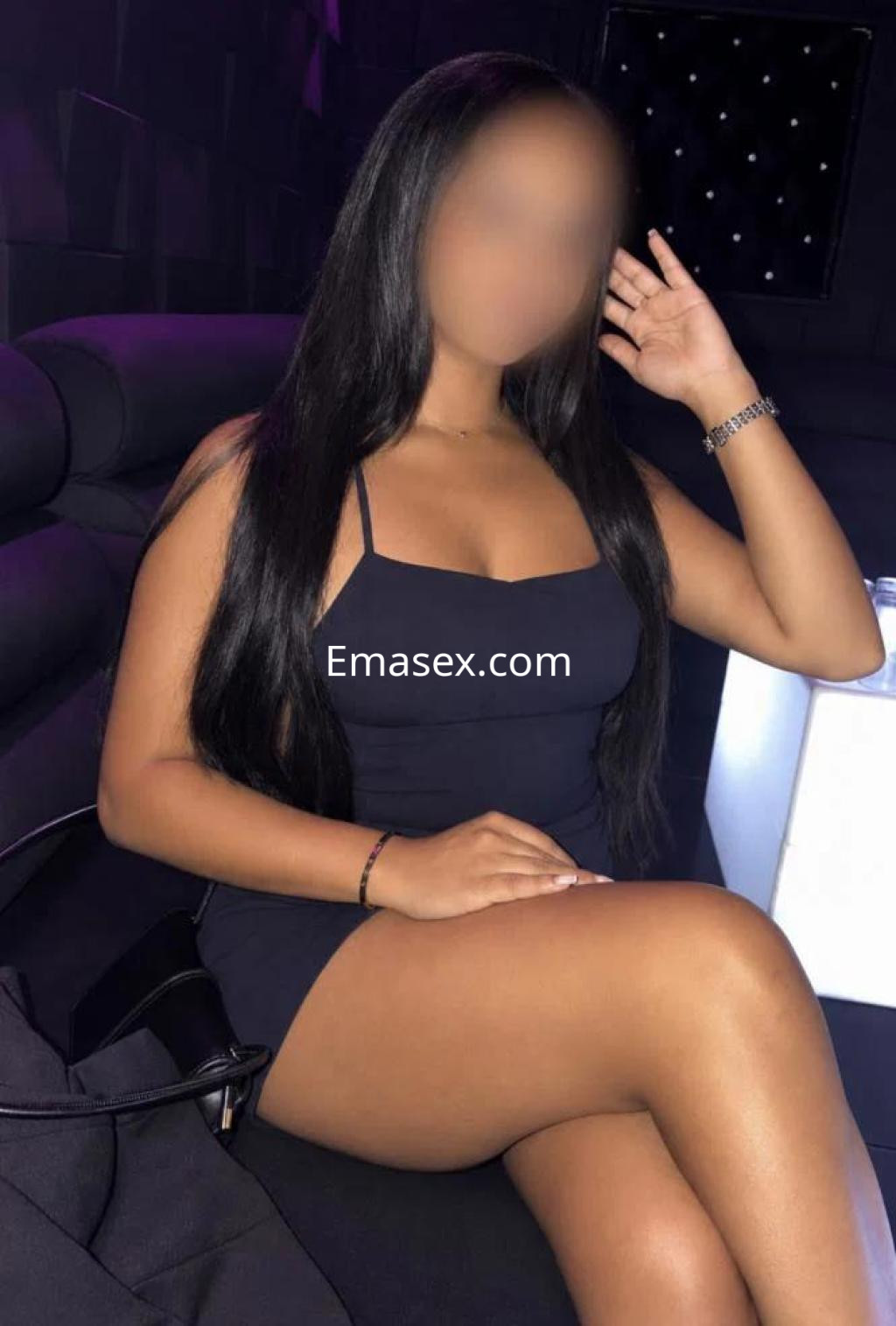 Escort en Tarragona con vestido negro ajustado, sentada en un sofá, mostrando una pose relajada y elegante.