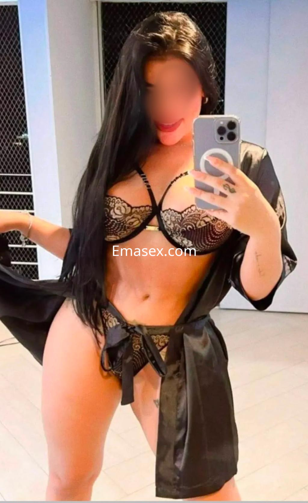 Escort en Granada mostrando su figura en un interior, vistiendo un conjunto de lencería negra con detalles dorados y una bata.