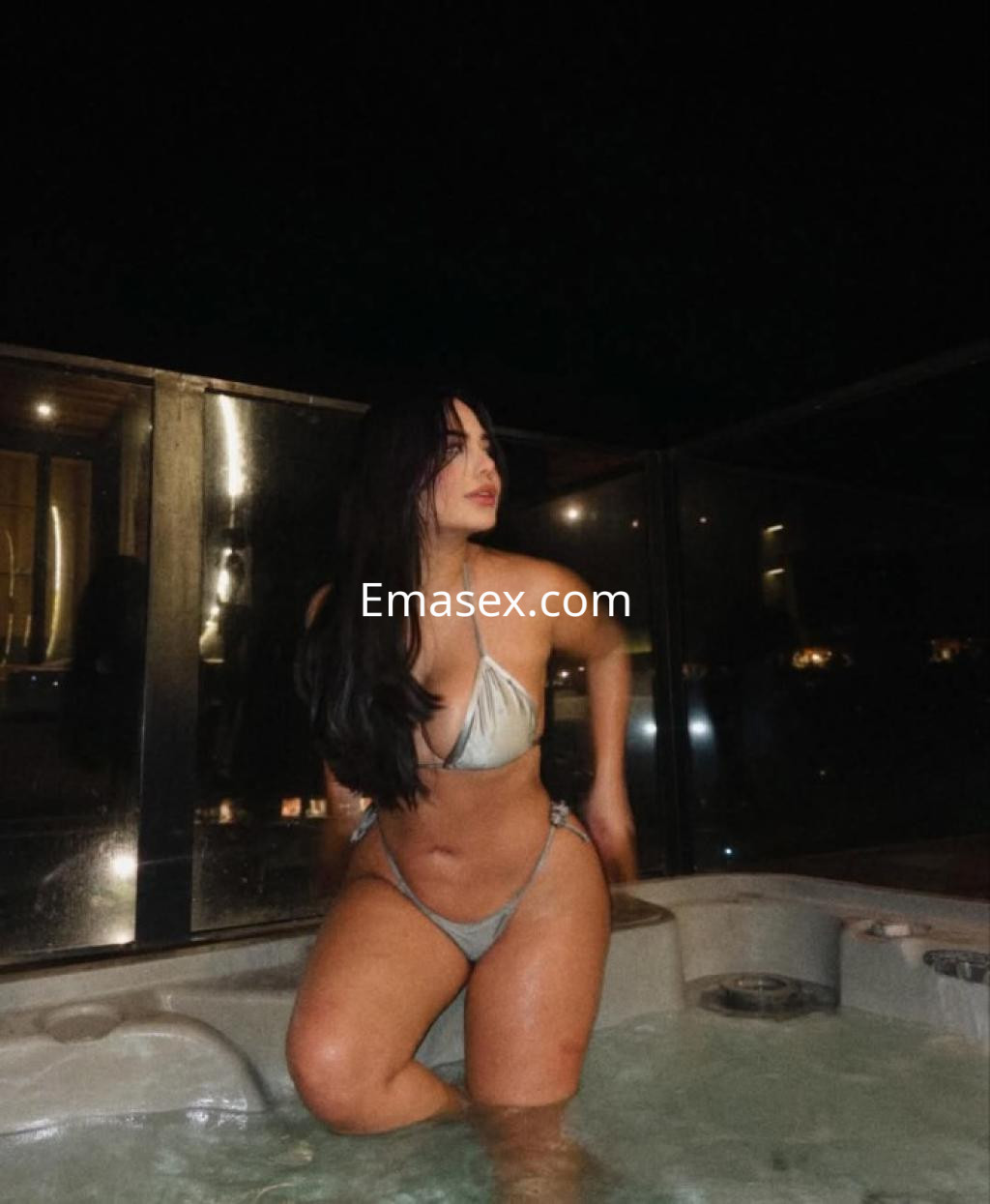 Escort en Pontevedra, luciendo un bikini claro mientras se relaja en un jacuzzi por la noche.