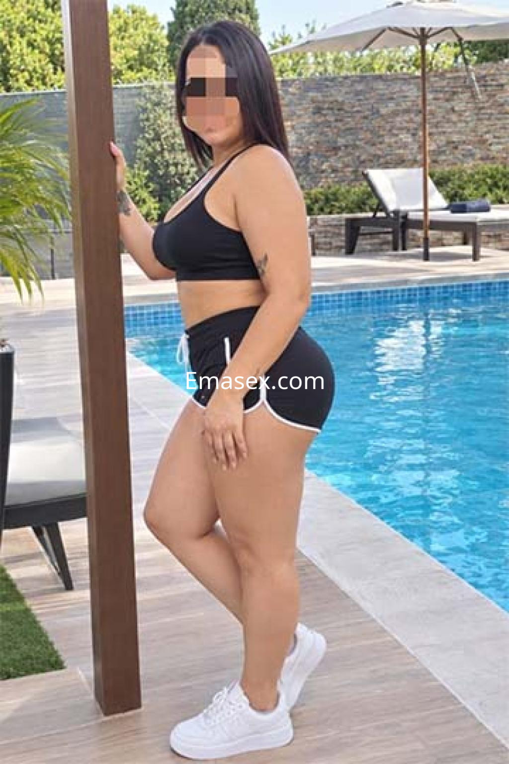 Puta en Logroño posa junto a una piscina, vistiendo un top negro y shorts cortos, con cabello lacio y oscuro.