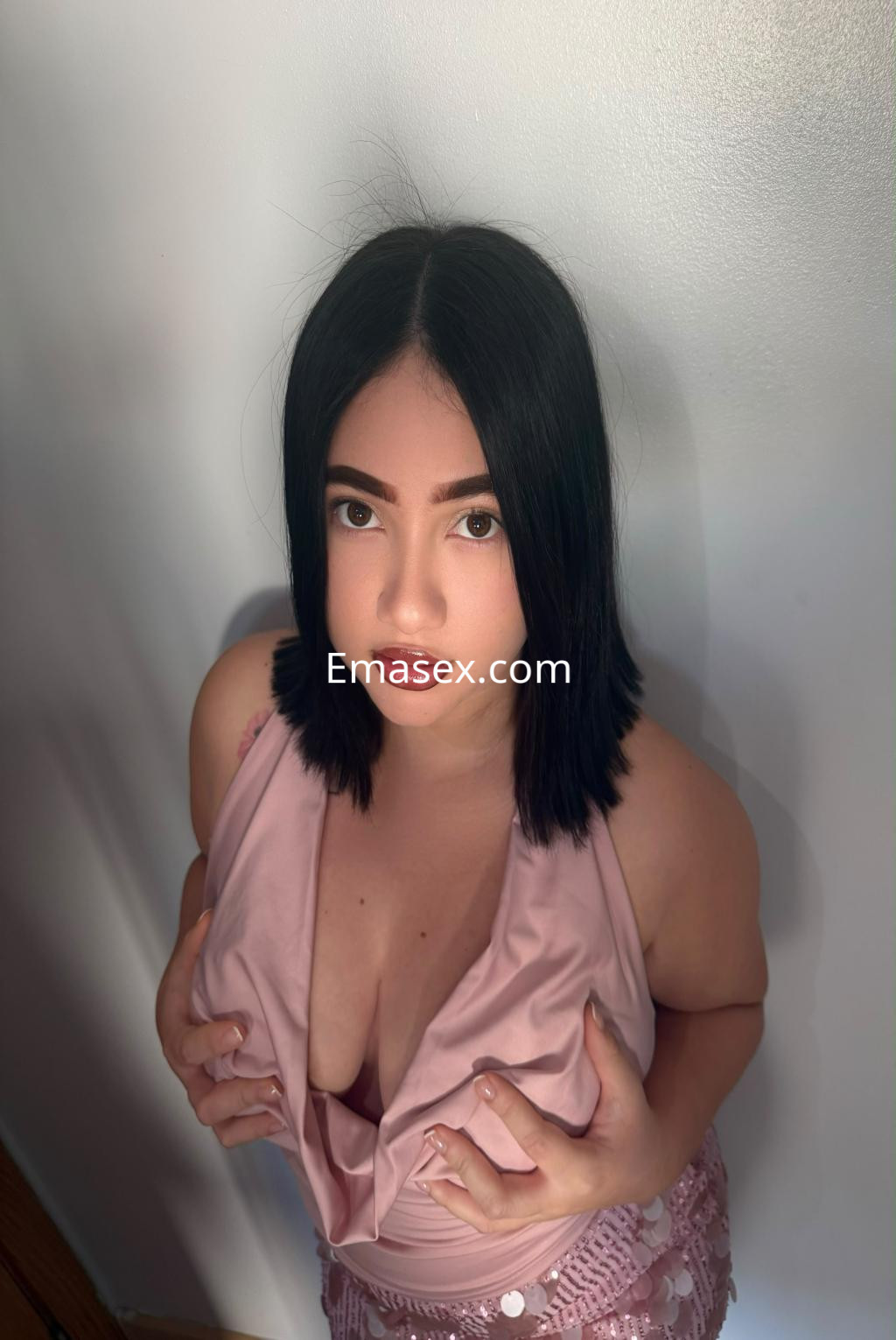 Escort en Irún con cabello lacio y oscuro, viste un top rosa que realza su figura, posando con una mirada cautivadora.