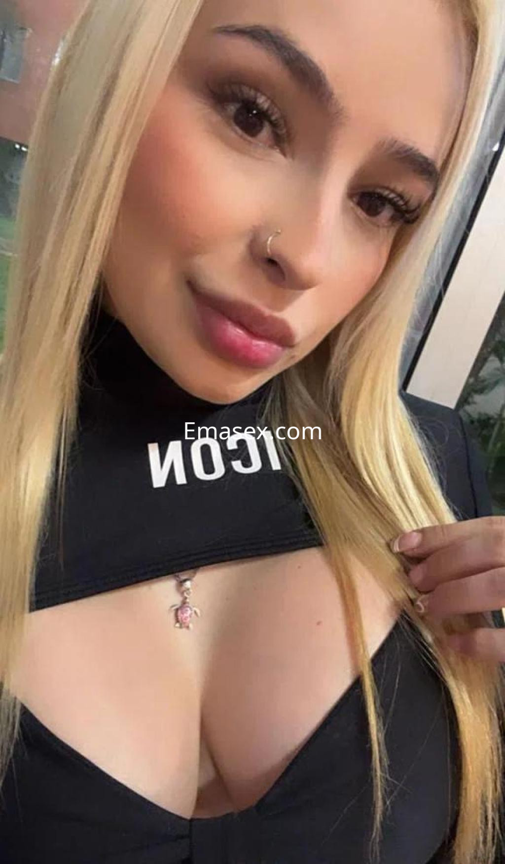 Escort en Málaga con cabello largo y rubio, vistiendo un top negro que resalta su figura y un piercing en la nariz.