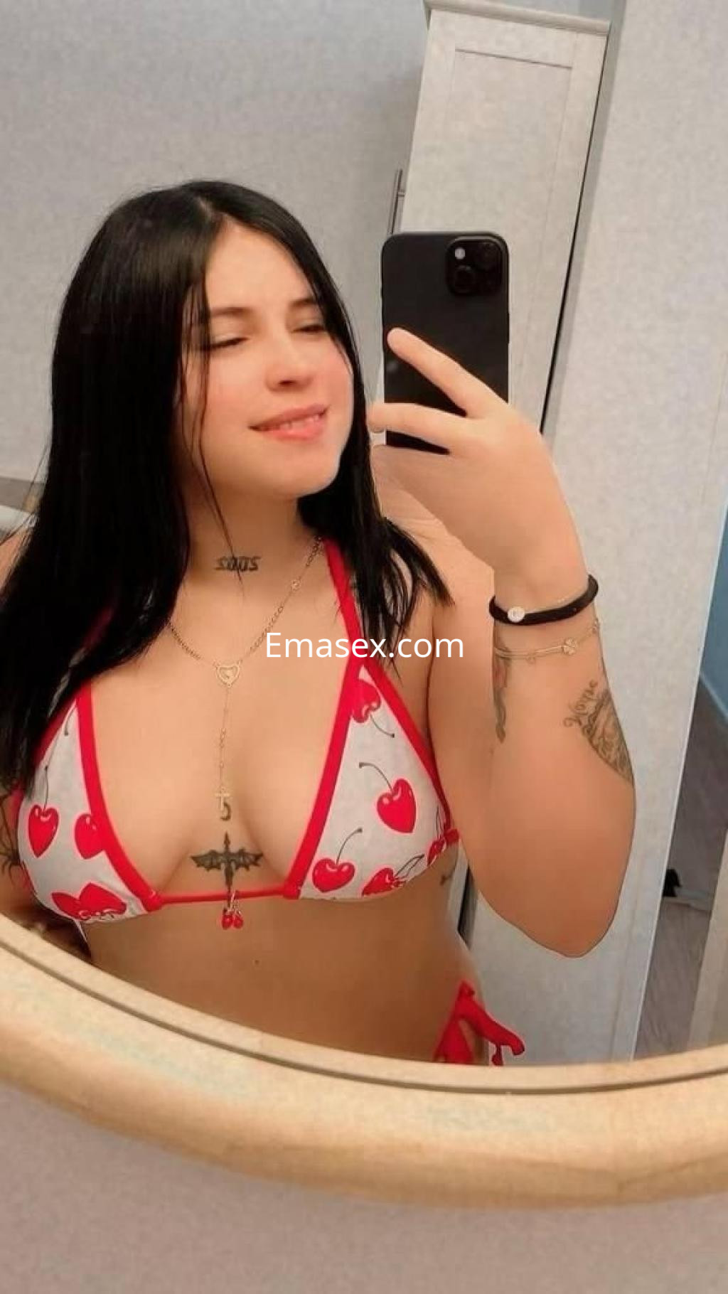 La puta luce un bikini rojo con estampado de cerezas, sonriendo mientras se toma una selfie en Málaga.