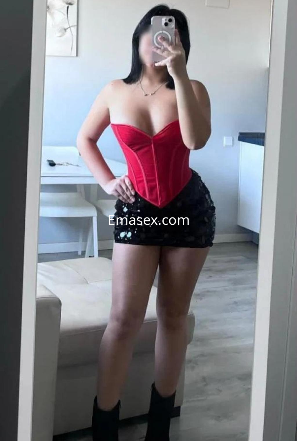 Puta en Cádiz posa frente al espejo con un corset rojo y una falda corta de lentejuelas negras, resaltando su figura.