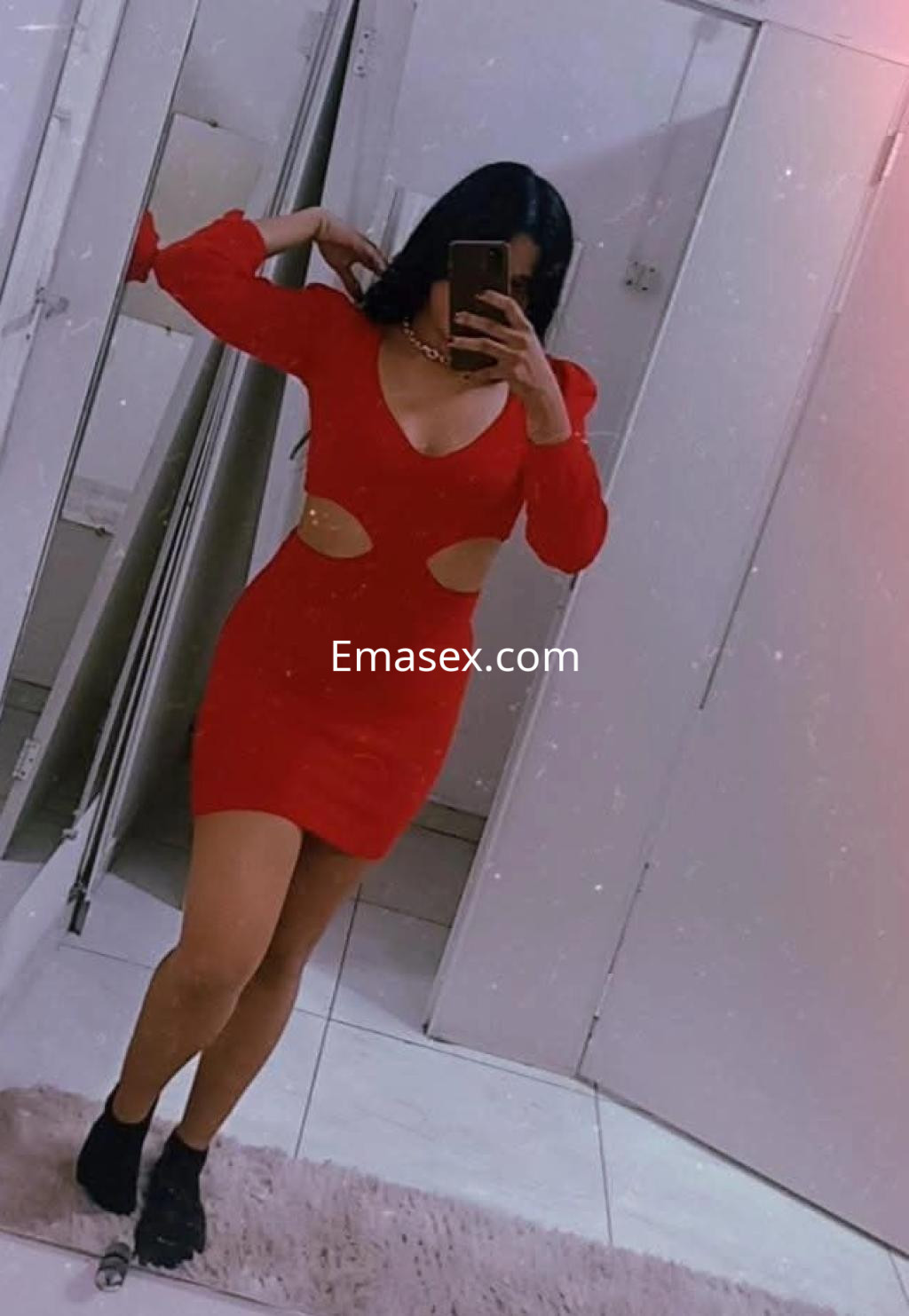 Escort en Gijón luciendo un vestido rojo ajustado con detalles cut-out, posando frente a un espejo.
