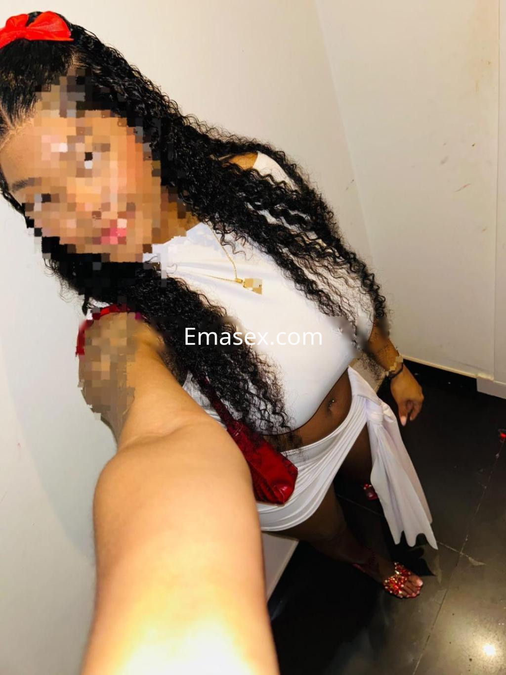 Escort con cabello rizado y oscuro, vistiendo un top blanco y una falda corta, posando en Lleida.