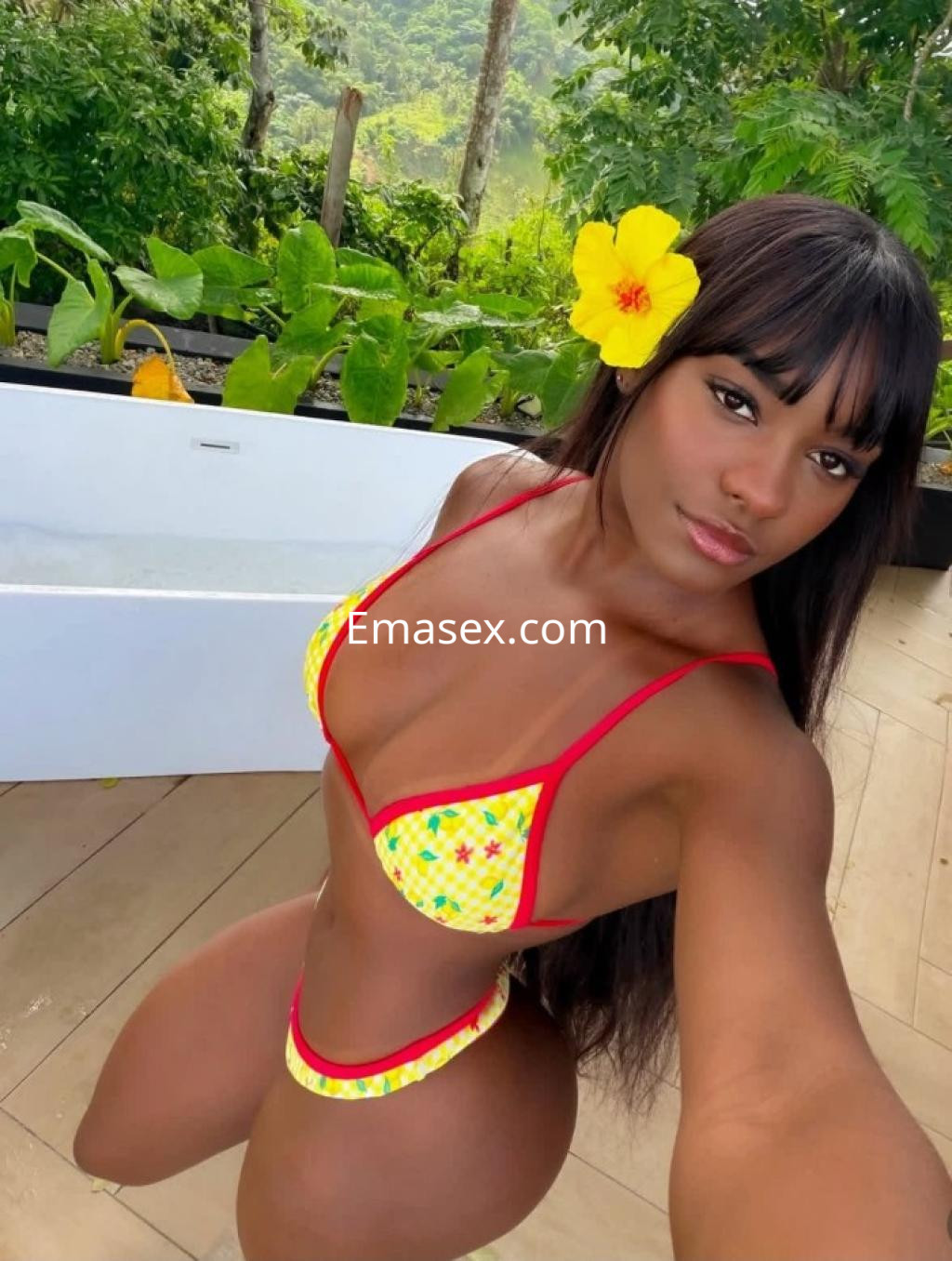 La puta posa con un bikini amarillo con detalles rojos y una flor en el cabello, en un entorno natural en Lugo.
