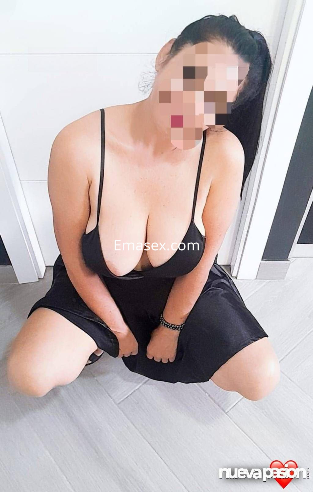 Escort en Cádiz luciendo un vestido negro ajustado, sentada en el suelo con el cabello recogido.
