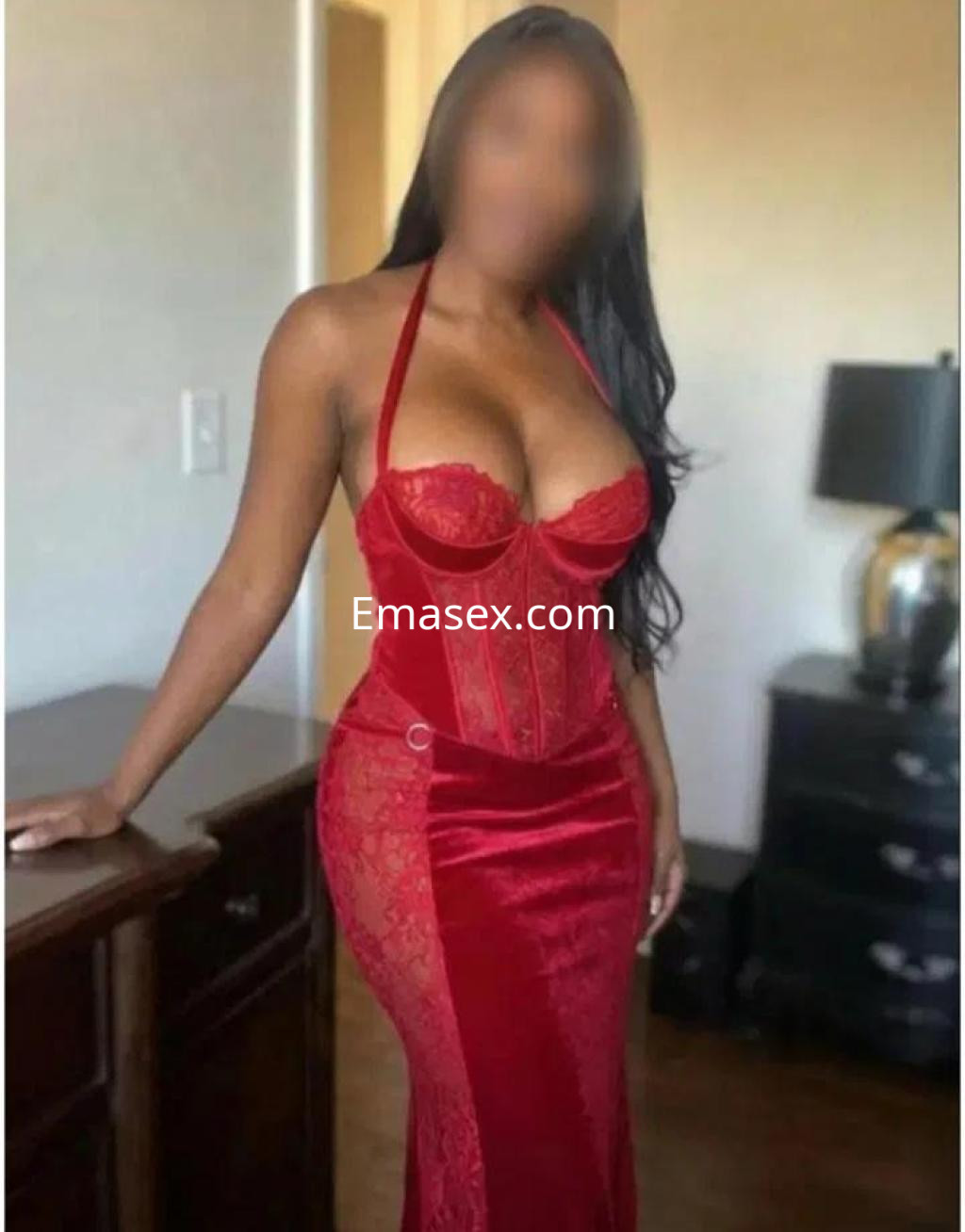 Puta en Pontevedra viste un ajustado vestido rojo de encaje, posando con confianza junto a un mueble.