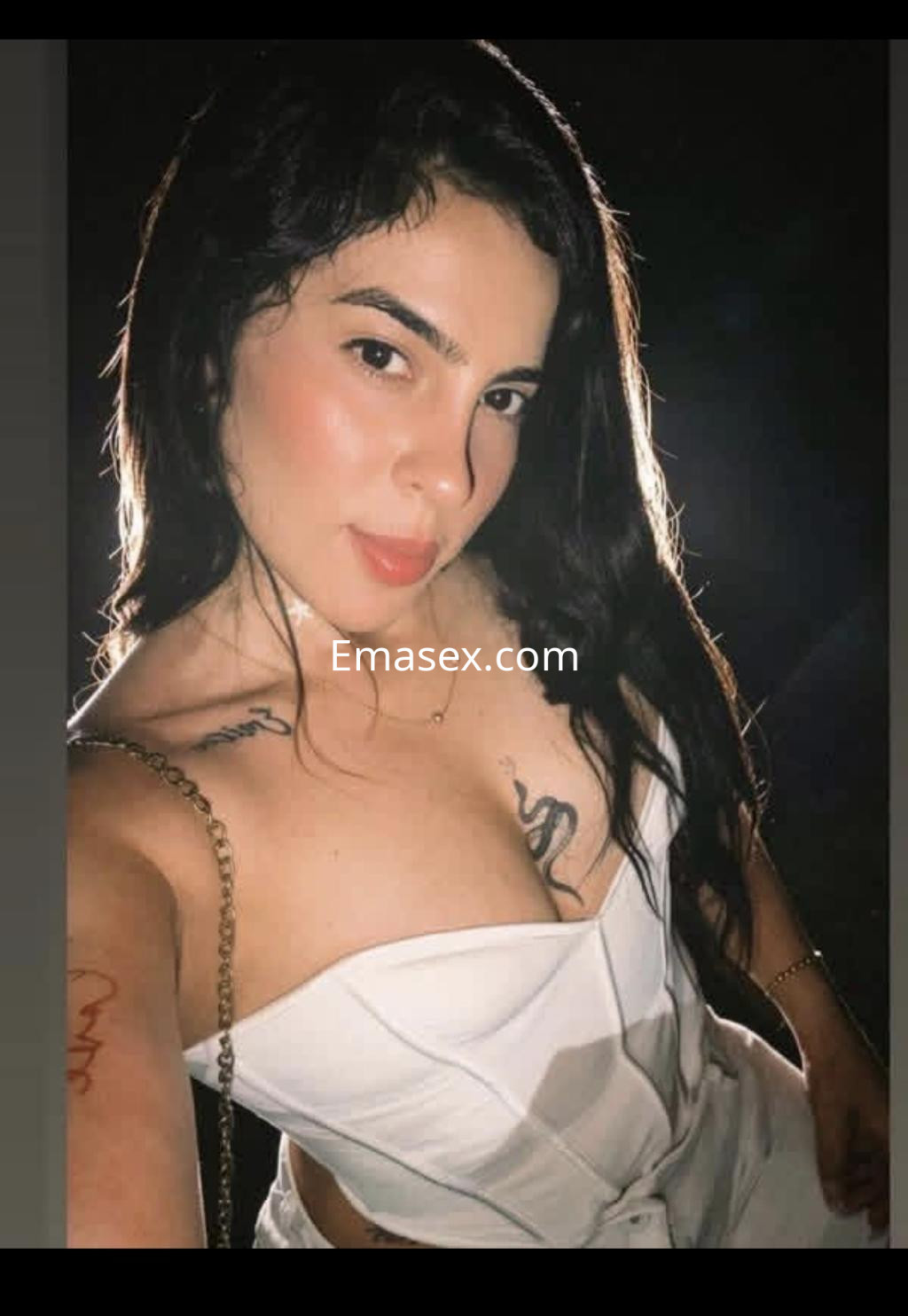 Puta en Bilbao posando con un vestido blanco ajustado, mostrando tatuajes y una expresión seductora.